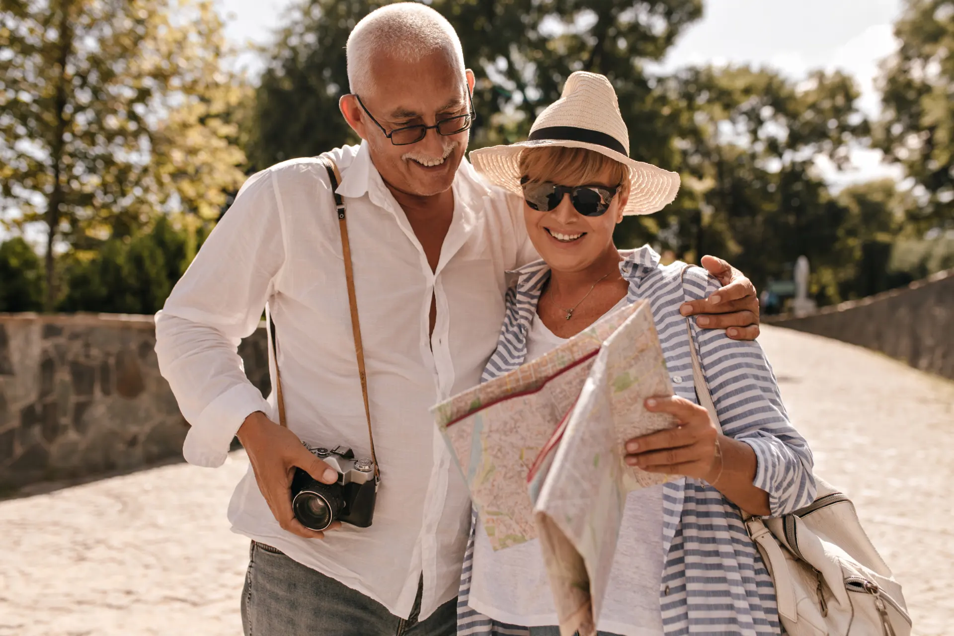 cheerful-man-with-grey-hair-light-shirt-jeans-with-camera-smiling-looking-map-with-blonde-lady-hat-blue-outfit-park